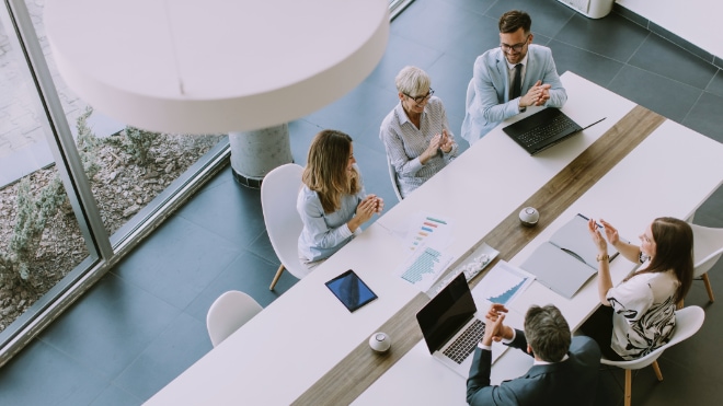 A team of profesional-looking people sit around a table, congratulating themselves.