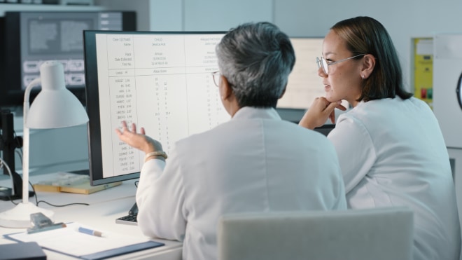 A medical team discuss performance data at their desktop computer.